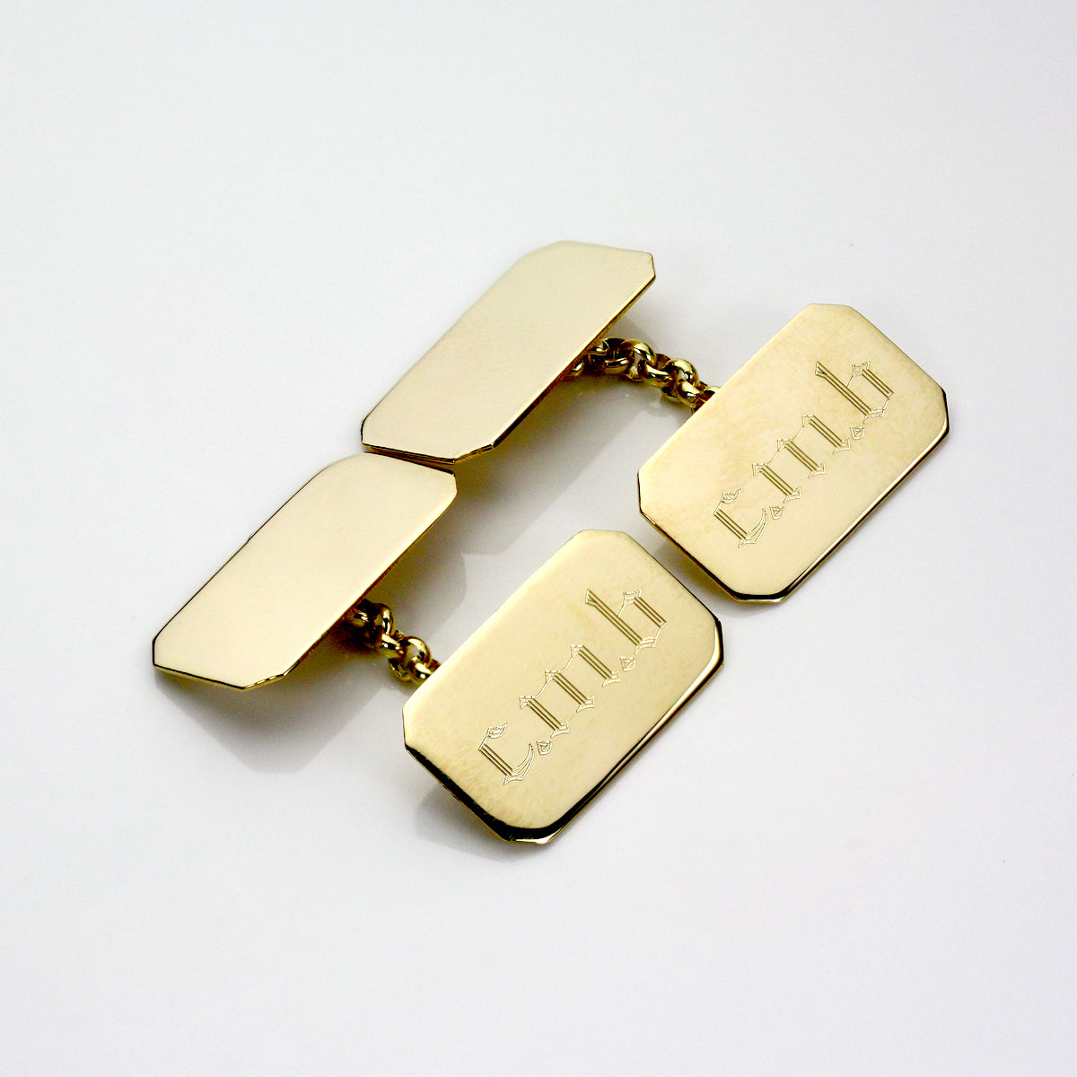 Gold rectangular cufflinks on a white background with cmb engraved on them in a gothic font